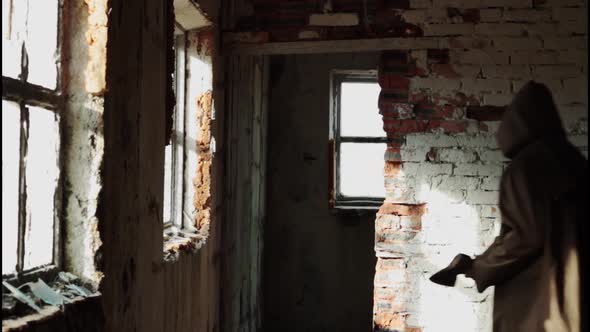 a Man in a Long Cloak with a Hood Walks in an Abandoned Building with Bloody Ax alt