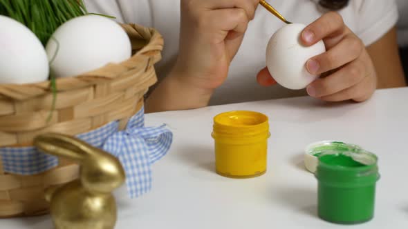 Children drawing on painted eggs at the table, at home. Preparing for the Easter holiday. alt