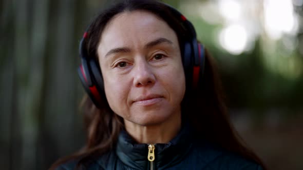 Portrait of Calm Pretty Woman with Wireless Headphones in Nature Lady is Walking and Enjoying Music alt