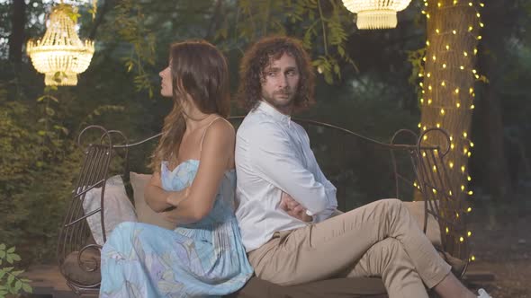 Side View of Argued Young Couple Sitting Back To Back with Hands Crossed. Loving Caucasian Man and alt