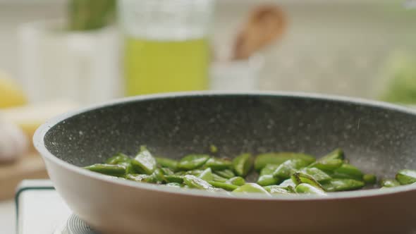 Crop woman putting green beans on plate in kitchen alt