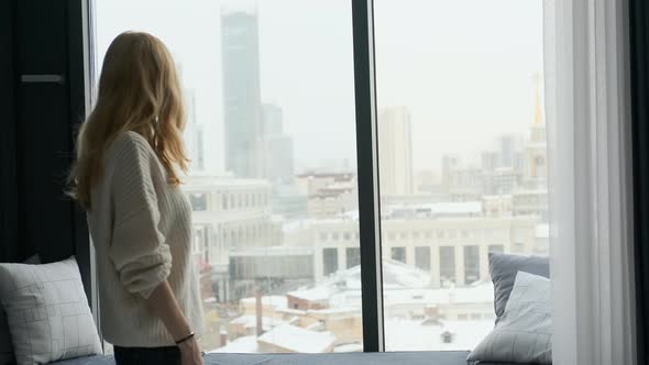 a woman comes to the window overlooking the city and raises her hands