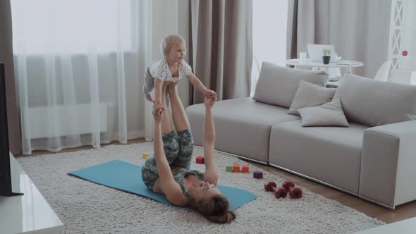 Mom Does Workout with Her Baby at Home. She Raises Her Baby on Her Feet While Lying on a Karemat alt