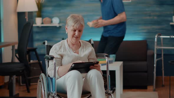 Aged Woman Using Digital Tablet While She Sits in Wheelchair alt