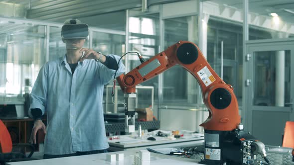 Male Developer in VR-glasses Is Working with High-tech Robot alt