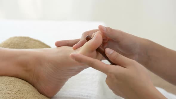 Therapist giving foot massage with stick to a woman in spa
