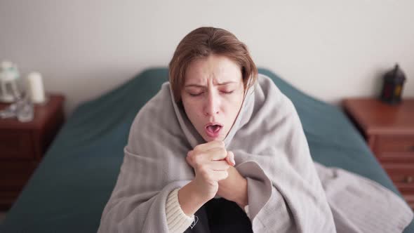An Unhealthy Young Woman with a Sore Throat and Fever Takes Cover with a Blanket in Bed in the