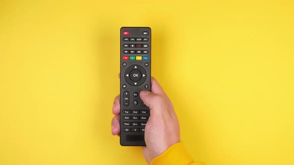 Male hand presses buttons on a black remote control from a smart tv on a yellow background