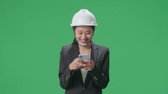 Smiling Asian Female Engineer Using Smartphone And Shaking Her Head In The Green Screen Studio alt