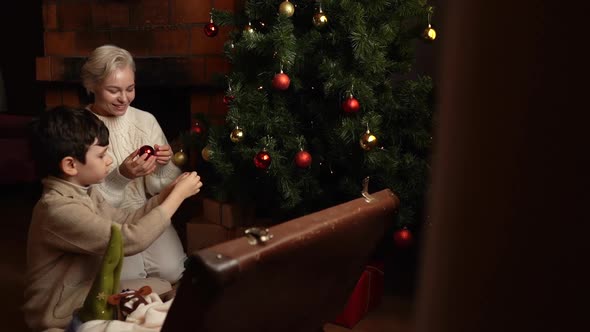 Joyful Young Mother and Pretty Son Boy Decorating with Colorful Balls of Christmas Tree Flashing alt