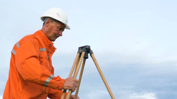 Professional Surveyor Puts Brown Wooden Tripod on Ground alt