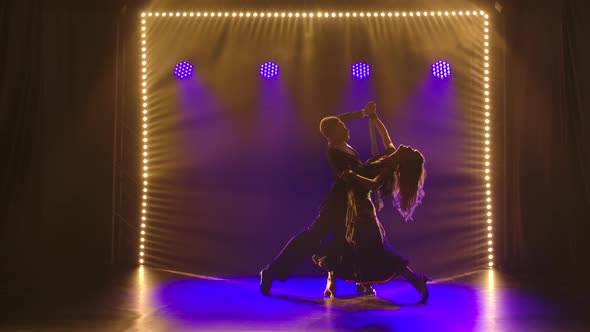 A Couple of Ballroom Dancers Are Spinning in a Waltz Against the Backdrop of Blue Lights. Silhouette alt