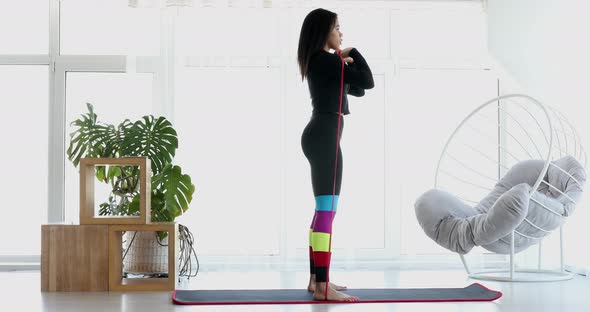 Black woman doing exercises using a fitness elastic band at home.