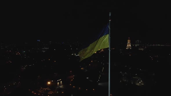 Aerial View of a Flag of Ukraine Flailing in the Wind at Night in Kyiv alt