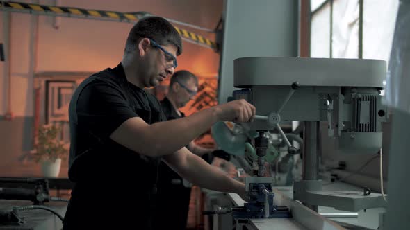 Professional workers drill a hole in a metal structure on a drilling machine in the production hall