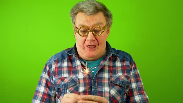 Caucasian Mature Adult Man Blows Hard on Sparkler and Wonders That He Cannot Extinguish It alt