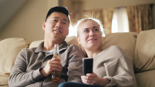 Young Multiethnic Family Watching Television Together, Man Drinking a Drink From a Bottle alt