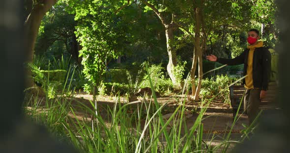 Two happy mixed race male friends walking and talking in park with backpacks alt