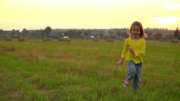 Camera Movement on Girl Runs and Laughs Across Field with Haystacks at Sunset
