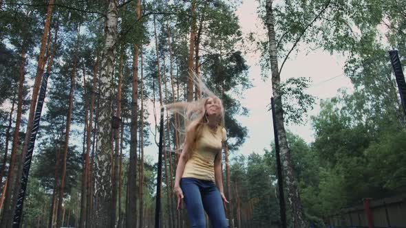 Happy Female Jumping on Trampoline. Beautiful Young Blond Barefoot Woman in Light Summer Shirt and alt
