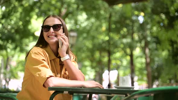 Serene Young Woman Talking on Mobile Phone Sitting in Summer Cafe Outside alt