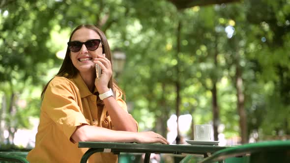 Serene Young Woman Talking on Mobile Phone Sitting in Summer Cafe Outside