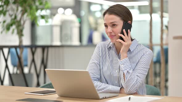 Young Woman with Laptop Talking on Smartphone in Office  alt