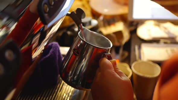 Close up on hands of coffee barista using coffee machine to add hot milk into silver jug alt