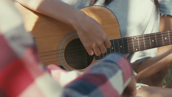 Close up hands Asian woman playing guitar happy with friends camping in nature.