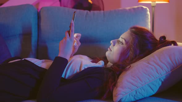 Young Woman Using Smartphone While Laying On Couch. alt