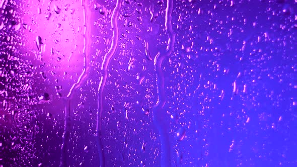 Raindrops of Water Flow Down the Glass in Rainy Weather on a Colored Pink Blue Blurred Background alt