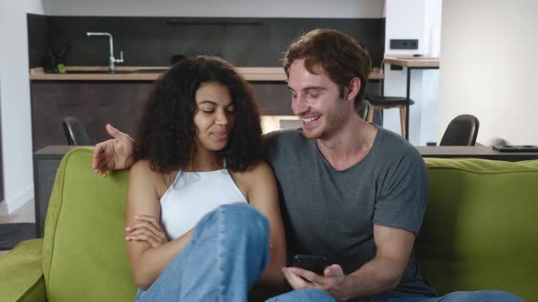 Beautiful Mixed-race Couple Have Fun, Flirt and Chat While Sitting on a Cozy Sofa at Home. Woman alt