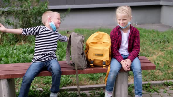 Back to School Girl and Boy Children Sit Talking on Bench Near the School Keeping Social Distance alt
