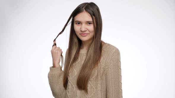Smiling Young Teenage Girl Twisting Long Hair on Finger and Looking in Camera alt