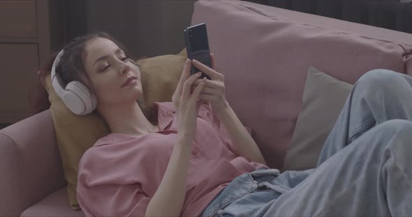 Girl Listens To Music With Headphones While Lying On The Couch And Looks Into A Smartphone