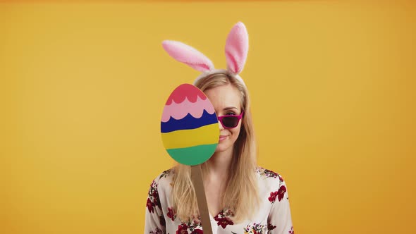 Humorous Caucasian Girl in Her 20s with Bunny Ears Cardboard Easter Egg and Sunglasses Posing at alt