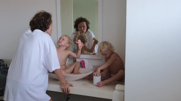 Mom with Children in the Bathroom Brushes Her Teeth in the Morning alt