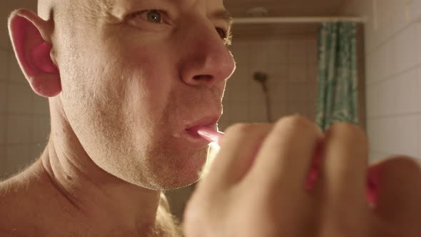 A man brushes his teeth towards a bathroom mirror alt