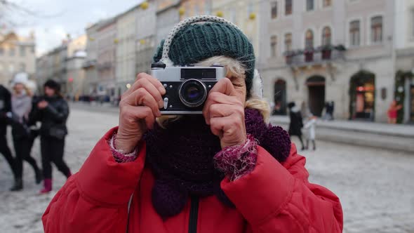 Senior Old Woman Tourist Taking Pictures with Photo Camera Using Retro Device in Winter City Center alt