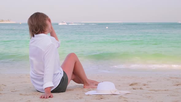 Attractive Lonely Girl Sitting on the Beach in the Shade and Looks to the Ocean alt