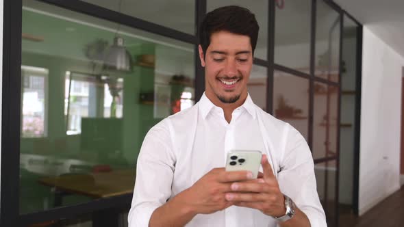Positive Hispanic Male Employee Using Smartphone for Online Communication