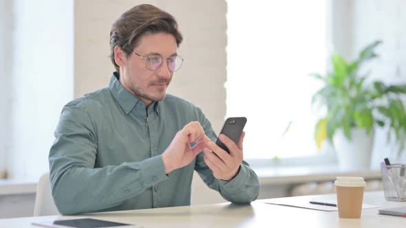 Attractive Middle Aged Man using Smartphone in Office alt