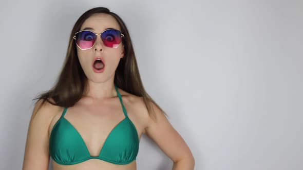 An attractive young slim sexy woman in a green bikini and sun glassless looking shocked