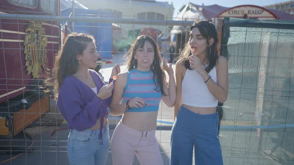 Three Happy Girls with Lollipops Stand and Joke Around By Metal Fence alt