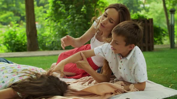 Boy and Girl Having Fun in Forest with Mother Outdoors. Family Lying on Blanket alt