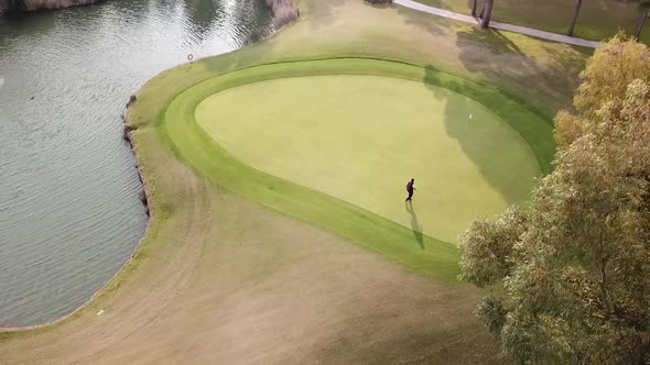 Golf player walking on green and vibrant golf field towards hole pole alt
