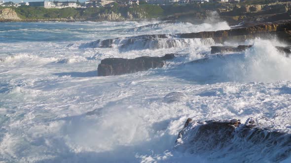 Tumultuous ocean waves crashing into rocks, shooting water straight up into the sky. alt