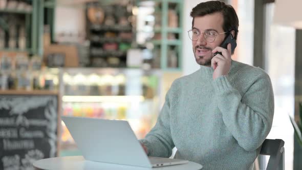 Young Man with Laptop Talking on Smartphone alt