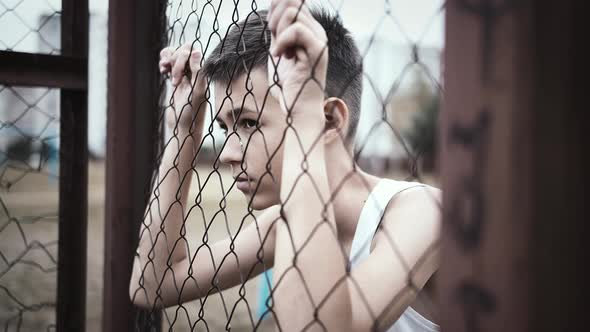 Cinematic Refugee Sad Boy Stands Alone Head Bowed Near the Fence Frustrated Boy Dropped Eyes