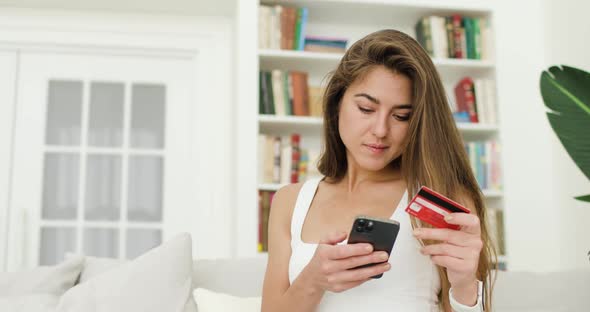 Portrait of Young Beautiful Woman Making Purchases Via the Internet Using a Smartphone and a Bank